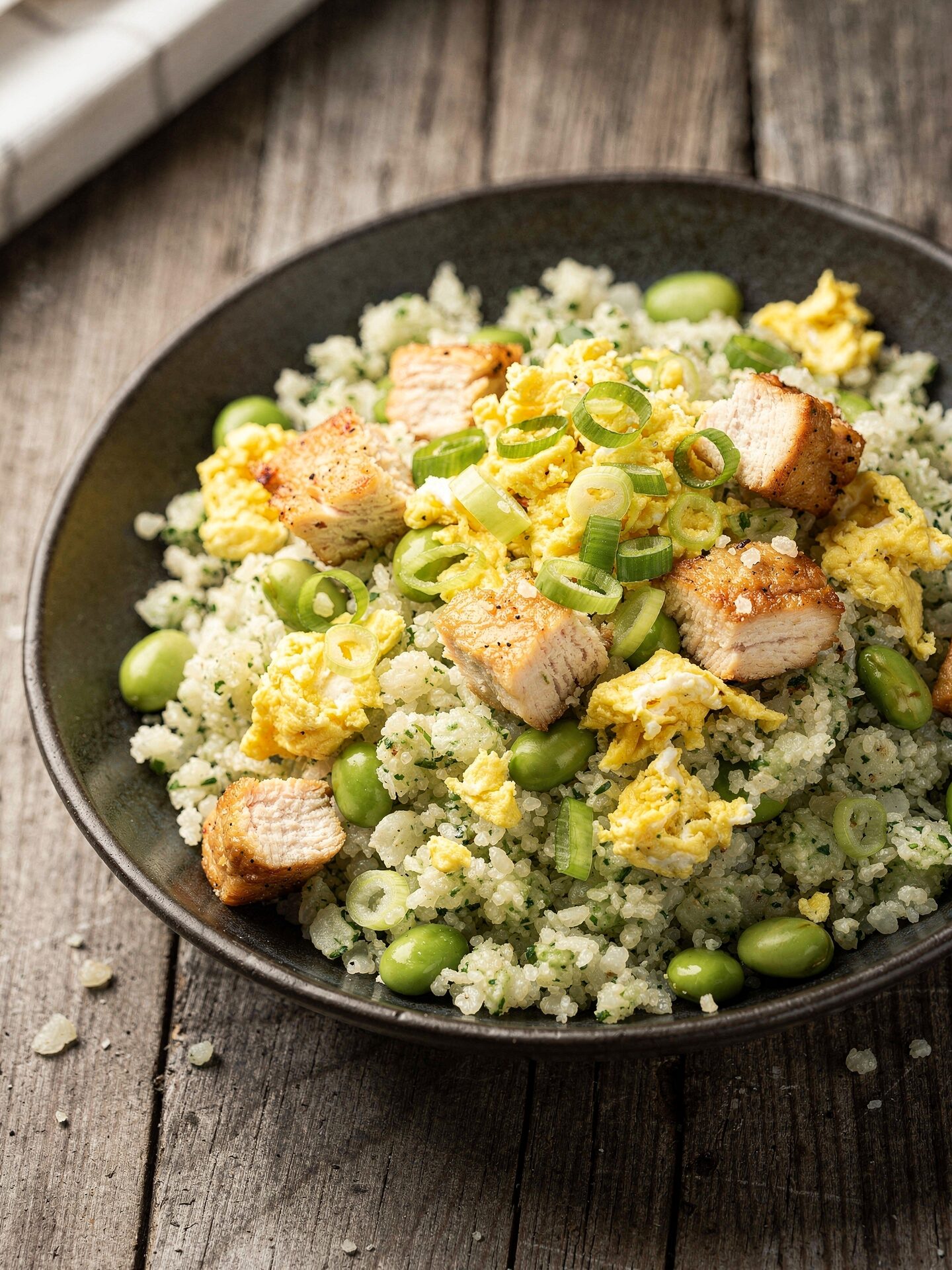 Bowl of high protein cauliflower rice with cubed chicken, edamame, scrambled egg and sliced green onions