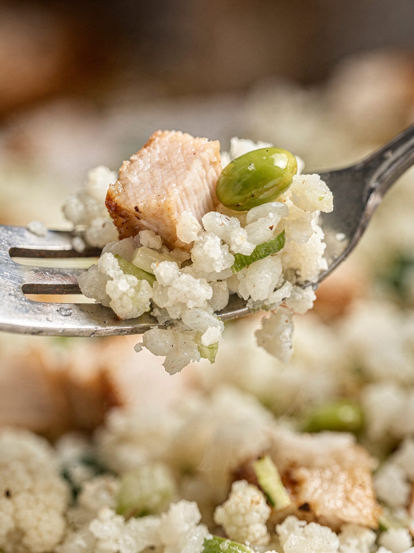 Close-up of a fork lifting cauliflower rice with chicken pieces and edamame showing the stir-fried texture